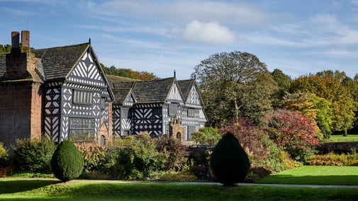 Black and white Tudor house from the side with autumn trees beyond